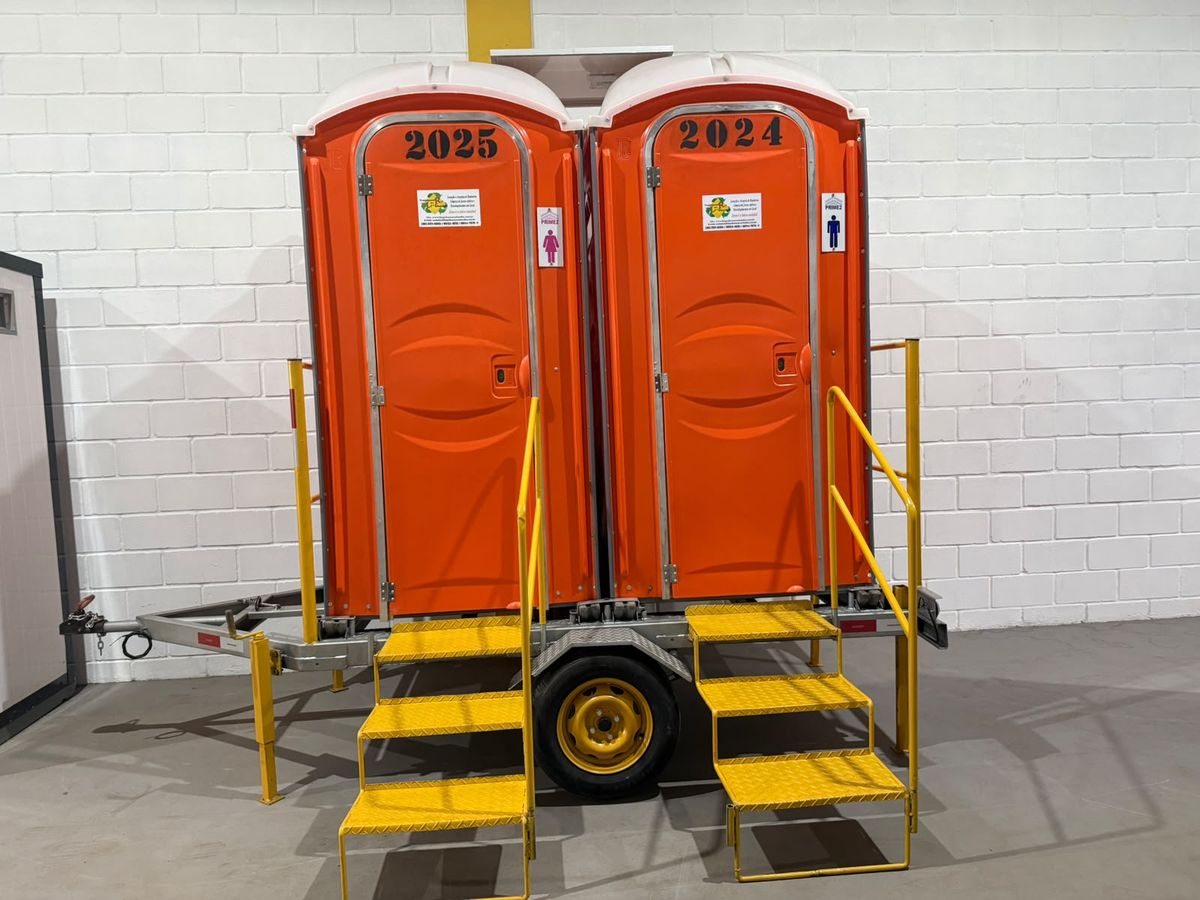 Duas cabines sanitárias laranja da LR Service montadas em reboque com escadas